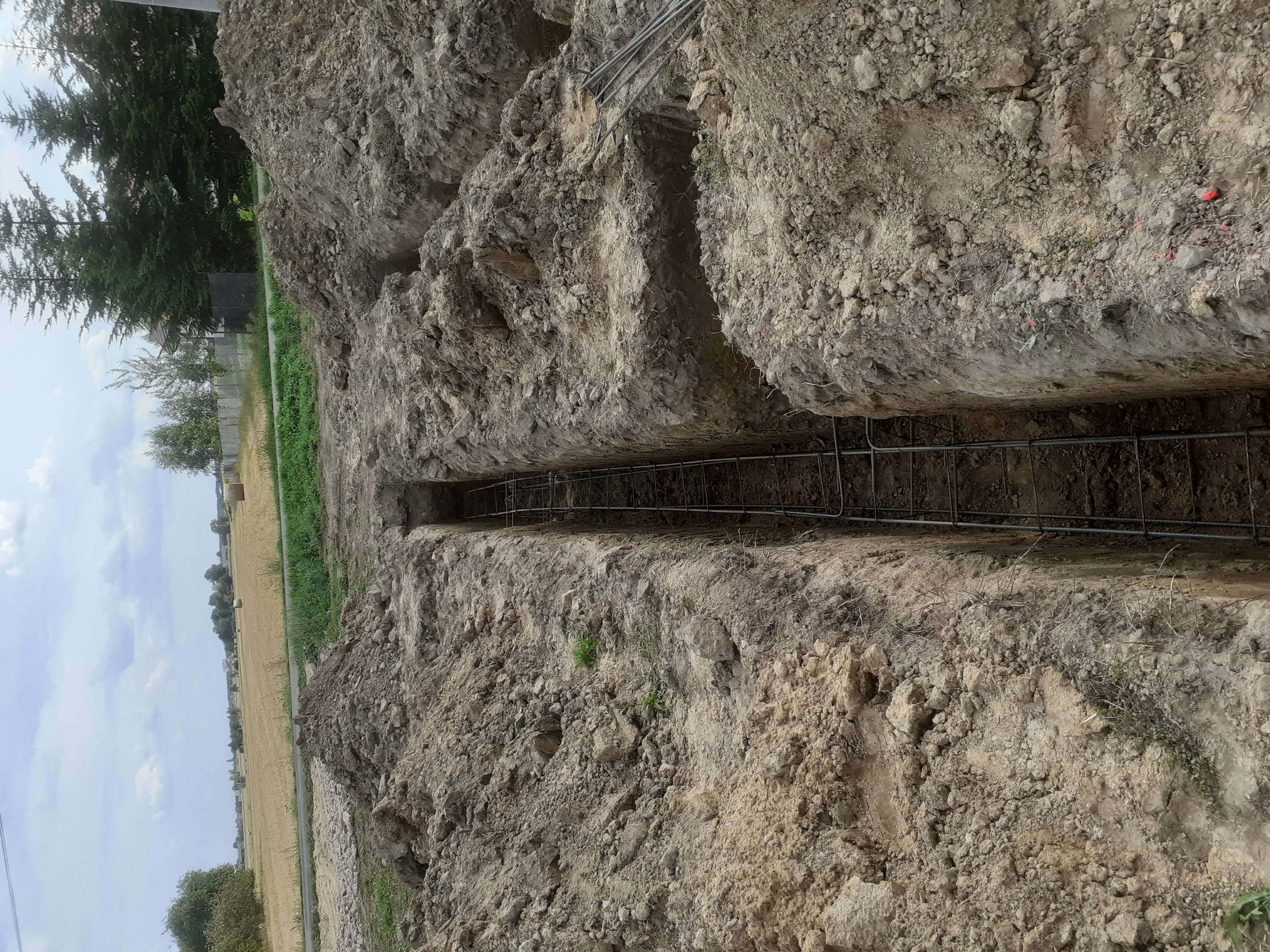 Wykop pod fundament z ułożonym zbrojeniem, widok z góry na ziemię, w tle pole i drzewa.