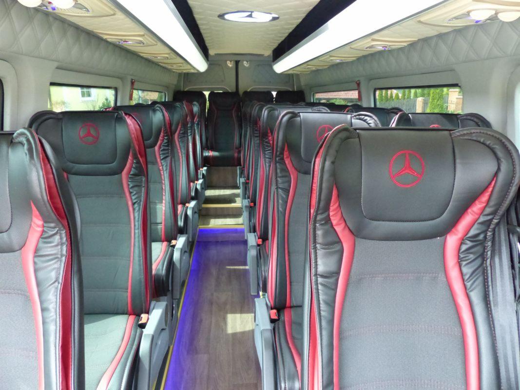 Wnętrze luksusowego busa z czarno-czerwonymi skórzanymi fotelami z emblematem, oświetleniem LED podłogi i podsufitką z pikowaniem w romby.