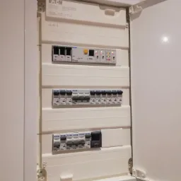 Otwarta, biała skrzynka elektryczna marki Eaton z widocznymi bezpiecznikami i modułem sterującym, zamontowana na ścianie wewnątrz pomieszczenia.