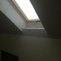 Montaż płyty gipsowo-kartonowej wokół okna dachowego, widoczne łączenia płyt i surowy stan wykończenia.