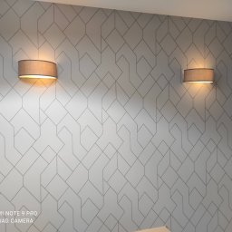 Usługi Ogólnobudowlane Mariusz Filip - Dwa identyczne, brązowe kinkiety z abażurami, emitujące ciepłe światło, zamontowane na ścianie pokrytej geometrycznym, szarym wzorem.