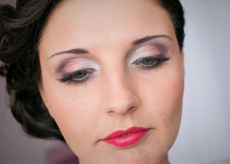 Portret kobiety z eleganckim, wieczorowym wykończeniem oczu w odcieniach różu i szarości oraz intensywnie różową pomadką. Włosy upięte w stylu retro.