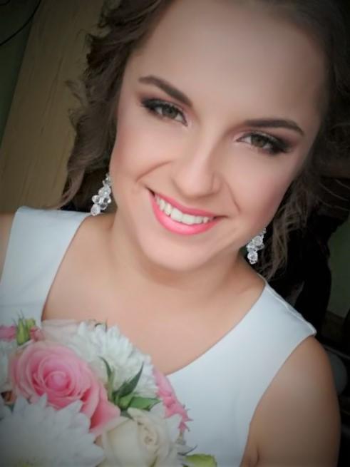 Uśmiechnięta panna młoda z bukietem różowych i białych kwiatów, prezentująca makijaż ślubny z mocno podkreślonymi oczami i różowymi ustami, oraz błyszczące kolczyki.