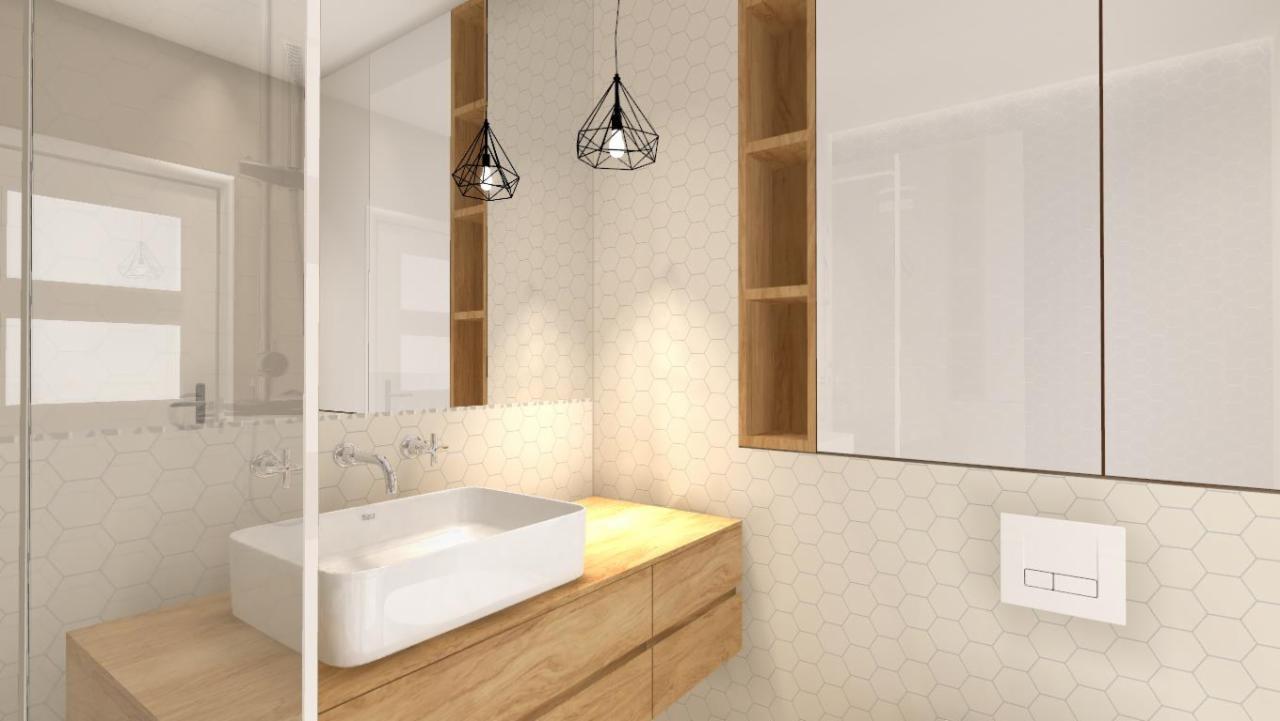 Nowoczesna łazienka z heksagonalnymi płytkami, drewnianą szafką pod umywalką i geometrycznymi lampami wiszącymi.