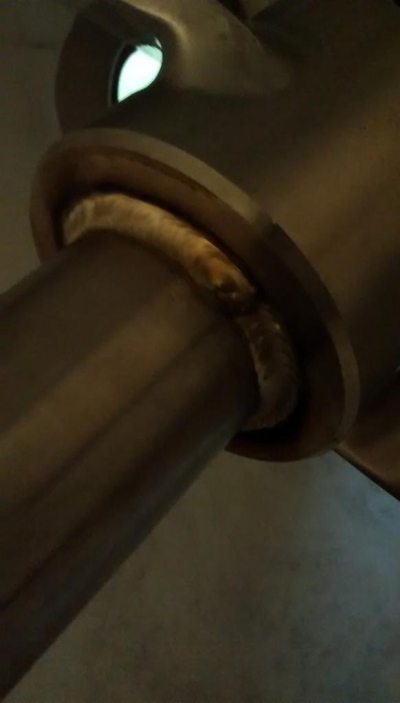 Spoina spawalnicza łącząca rurę z kołnierzem, widoczna z bliska, oświetlona sztucznym światłem, ukazująca precyzję i jakość wykonania.