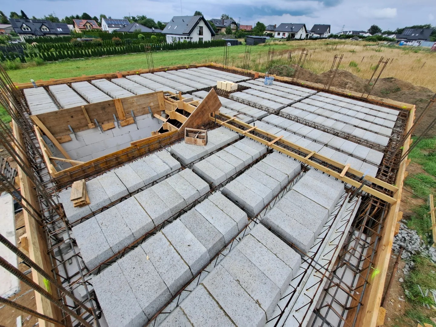 Wiązanie zbrojenia i układanie pustaków szalunkowych na stropie w trakcie budowy domu jednorodzinnego, widoczne drewniane szalunki i wystające pręty zbrojeniowe.
