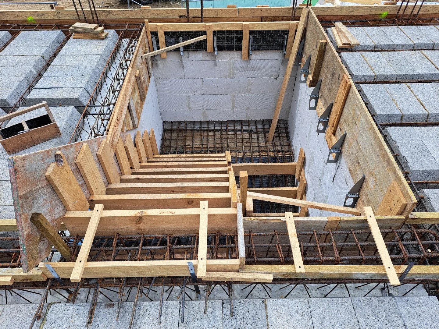 Szczegółowe ujęcie szalunku schodów zbrojonych, widoczne bloczki betonowe, stalowe pręty zbrojeniowe i drewniane elementy konstrukcyjne.