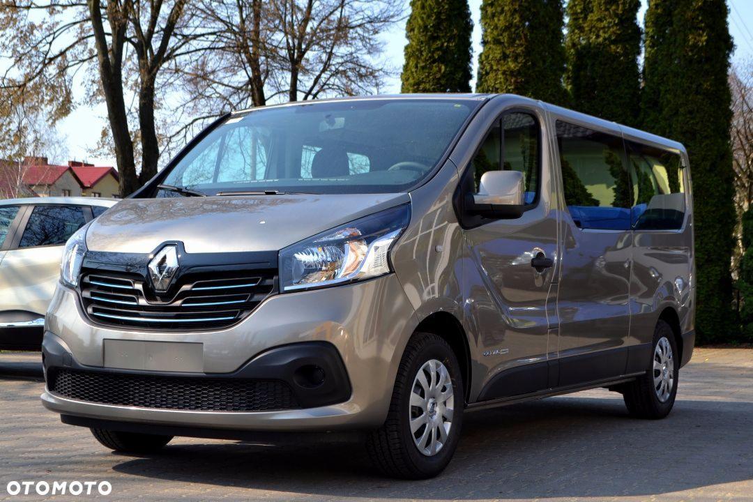 Szary Renault Trafic z niebieskimi siedzeniami pasażerskimi, sfotografowany z zewnątrz na tle drzew.