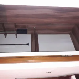 Wnętrze szafy wnękowej z drążkiem na ubrania, drewniane wykończenie w odcieniach brązu i bieli, widok z dołu.