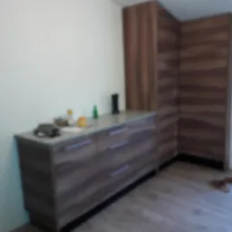 Komoda z szufladami i szafa narożna w kolorze drewna, widoczne akcesoria na blacie, podłoga wyłożona panelami.