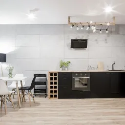 Nowoczesna kuchnia z czarnymi frontami, drewnianym blatem i stołem z krzesłami w stylu skandynawskim, oświetlona dekoracyjną lampą z żarówkami Edison