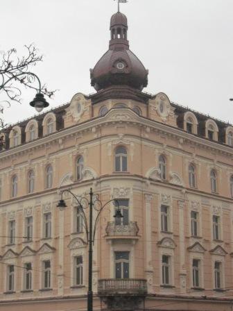 Fasada kamienicy w Uszwi z licznymi oknami i balkonem, zwieńczona kopułą z zegarem, widziana spod latarni.