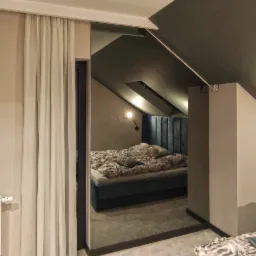 Nowoczesna sypialnia na poddaszu z łóżkiem z welurowym zagłówkiem, widoczna przez szerokie drzwi z zasłonami, z fragmentem drugiego łóżka na pierwszym planie.