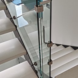 RAVATTI - Szklana balustrada zamocowana na schodach z podświetleniem LED, widok z góry, z elementami mocującymi w kolorze szczotkowanego mosiądzu.