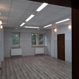 DR. House - Odnowione wnętrze biura w Białymstoku, widok na świeżo pomalowane ściany w odcieniach szarości, drewnopodobną podłogę, grzejniki pod oknami i nowoczesne oświetlenie sufitowe.