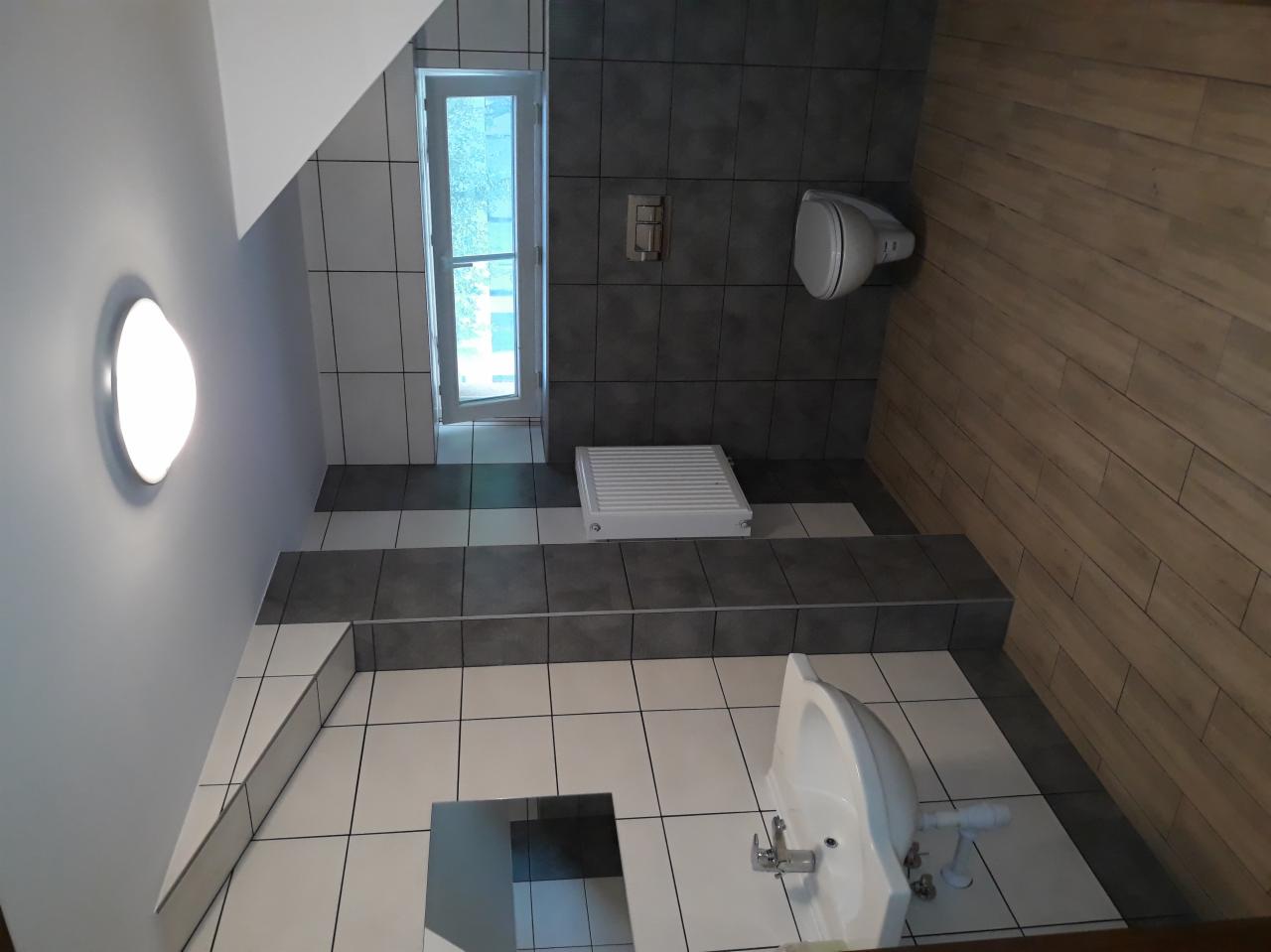 Wykończona łazienka z biało-szarą glazurą, drewnopodobną ścianą, grzejnikiem i sanitariatami, widok z góry.