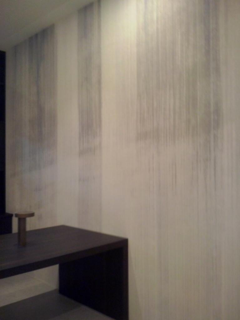 Ściana z tapetą o pionowych, rozmytym wzorze w odcieniach szarości i bieli, obok ciemny, minimalistyczny stolik.