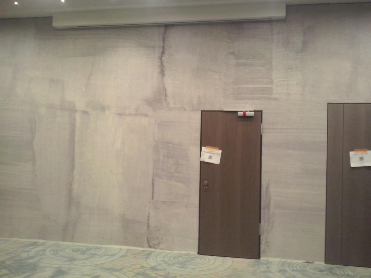 Ściana w biurze po szpachlowaniu, z widocznymi śladami po wałku, przygotowana do malowania, z dwiema drewnianymi drzwiami w tle z kartkami przyklejonymi do nich.