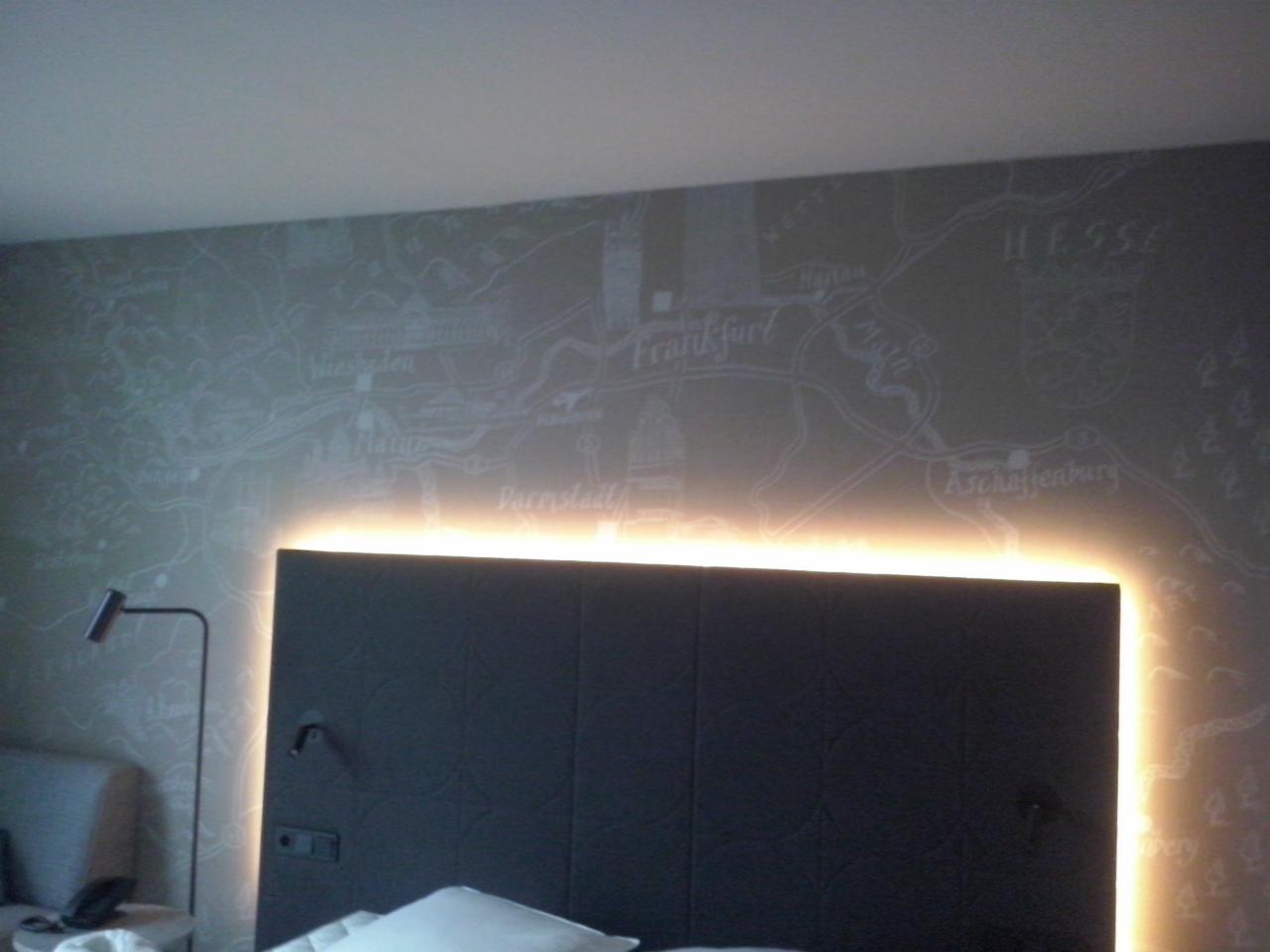 Pokój hotelowy z tapetą w mapę Hesji, podświetlony zagłówek łóżka i lampka nocna