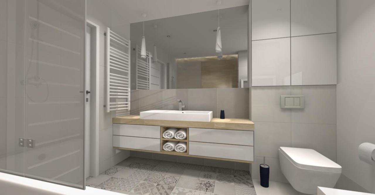 Jasna łazienka z kabiną prysznicową, umywalką na szafce z drewnianym blatem, wiszącą toaletą i mozaikową podłogą.