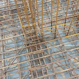 Zbrojenie fundamentu z pionowymi prętami i siatką z drutu wiązałkowego na czarnej folii hydroizolacyjnej.