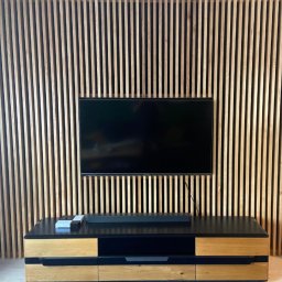Stolarstwo Zakład PHU Jarosław Jurek - Drewniana ściana z pionowych listew za telewizorem i szafką RTV. Naturalne drewno, nowoczesny design, minimalistyczny styl. Widoczne kable.