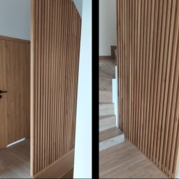 Stolarstwo Zakład PHU Jarosław Jurek - Nowoczesna aranżacja wnętrza: drewniana ściana lamelowa przy schodach i drzwiach, jasne drewno, minimalistyczny design, subtelne oświetlenie.