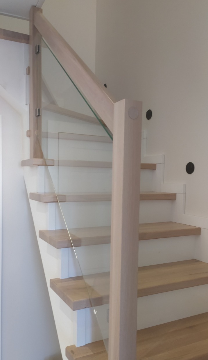 Jasne schody z drewnianymi stopniami i szklaną balustradą, widok z dołu, minimalistyczny design, oświetlenie punktowe na ścianie.