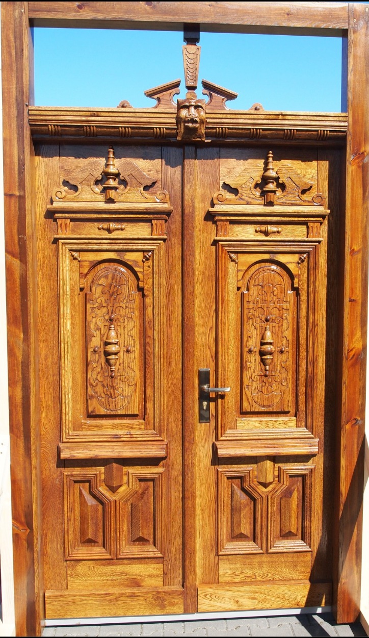 Bogato zdobione, dwuskrzydłowe drzwi z litego drewna o ciepłym, miodowym odcieniu. Rzeźbione detale i dekoracyjny motyw twarzy nadają im unikalny, klasyczny charakter.