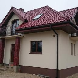 Zakład Ogólnobudowlany ZEN- BUD Zenon Kuźnik - Dwupiętrowy dom jednorodzinny z czerwonym dachem, beżową elewacją i balkonami z czarną balustradą, widok z zewnątrz w pochmurny dzień.