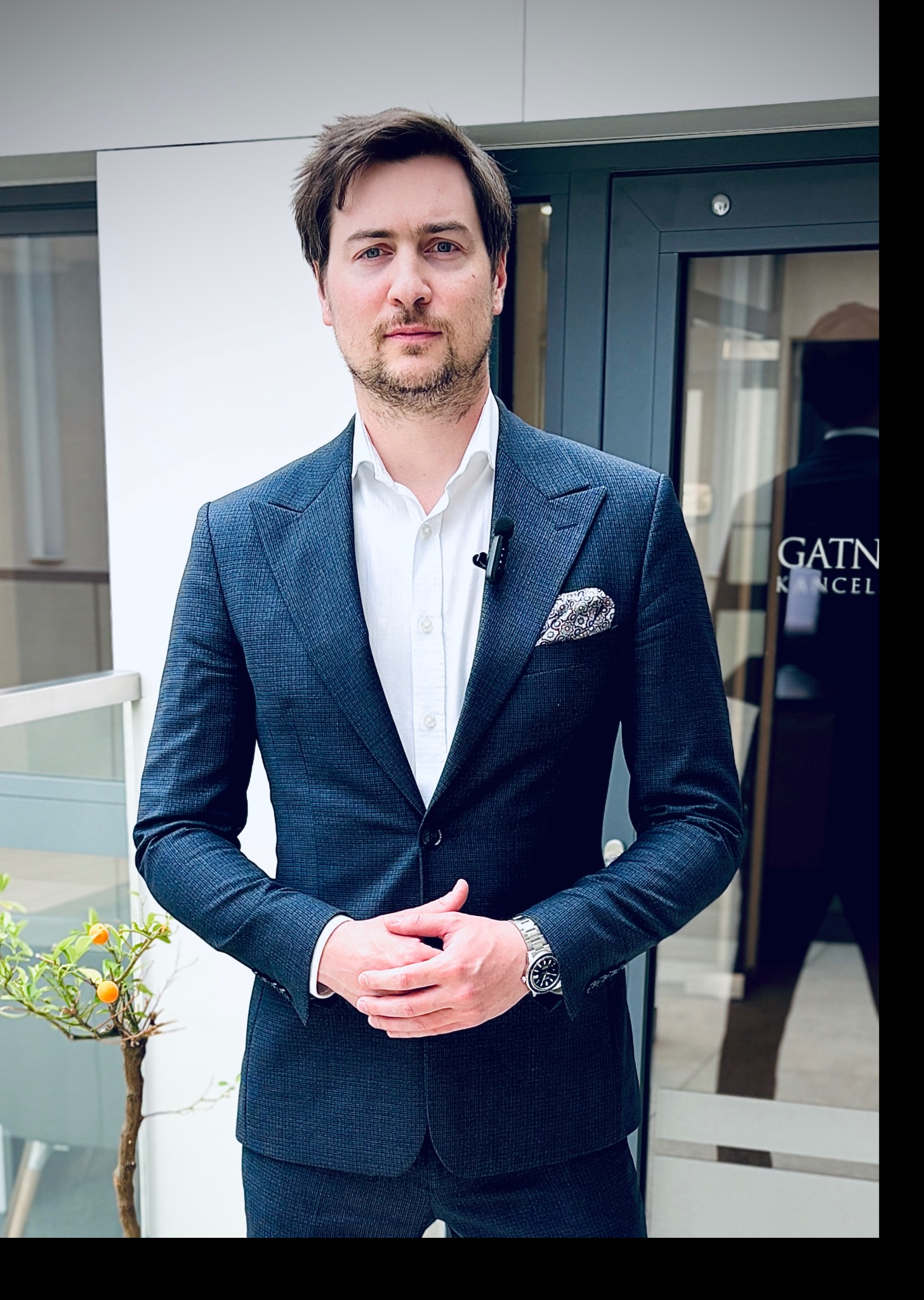 Adwokat Gabriel Gatner w Katowicach, w granatowym garniturze, prezentuje się profesjonalnie na tle drzwi z nazwą kancelarii.