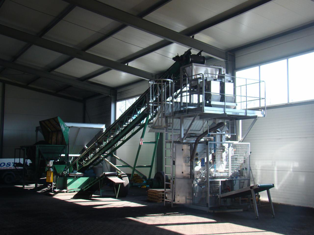 Linia produkcyjna do pakowania pelletu w hali w Krzeszowicach, z widocznym podajnikiem taśmowym i urządzeniem pakującym.