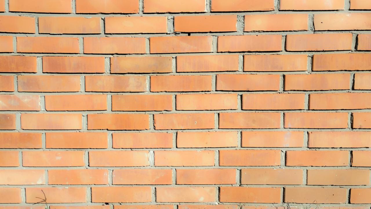 Fragment nowej ściany z cegły klinkierowej w odcieniach pomarańczy, spoiny szare, widoczne delikatne nierówności i różnice w kolorze cegieł.