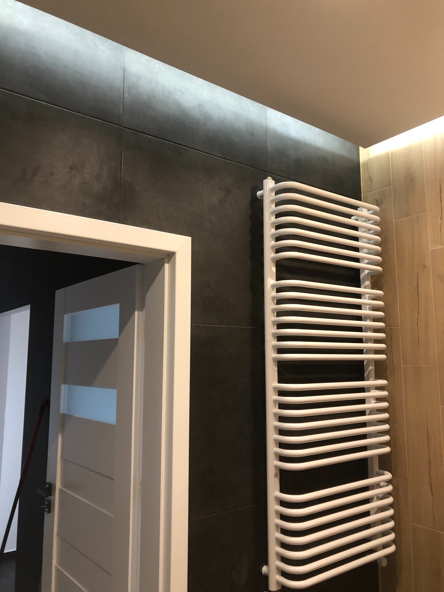 Nowoczesna łazienka z ciemnoszarymi płytkami, białą drabinką grzejnikową i białymi drzwiami z przeszkleniami.