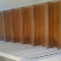 Konstrukcja schodów z drewnianymi stopniami i białą, pomalowaną ramą, widok od dołu, w trakcie montażu.