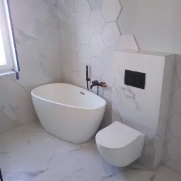 Nowoczesna łazienka z wolnostojącą białą wanną, wiszącą toaletą i heksagonalnymi płytkami na ścianie, wykończona marmurowymi płytkami podłogowymi i czarną armaturą.