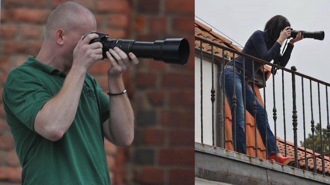 Dwie osoby z dużymi obiektywami fotografują z różnych perspektyw, mężczyzna przy ceglanej ścianie, kobieta na balkonie z pomarańczową dachówką.