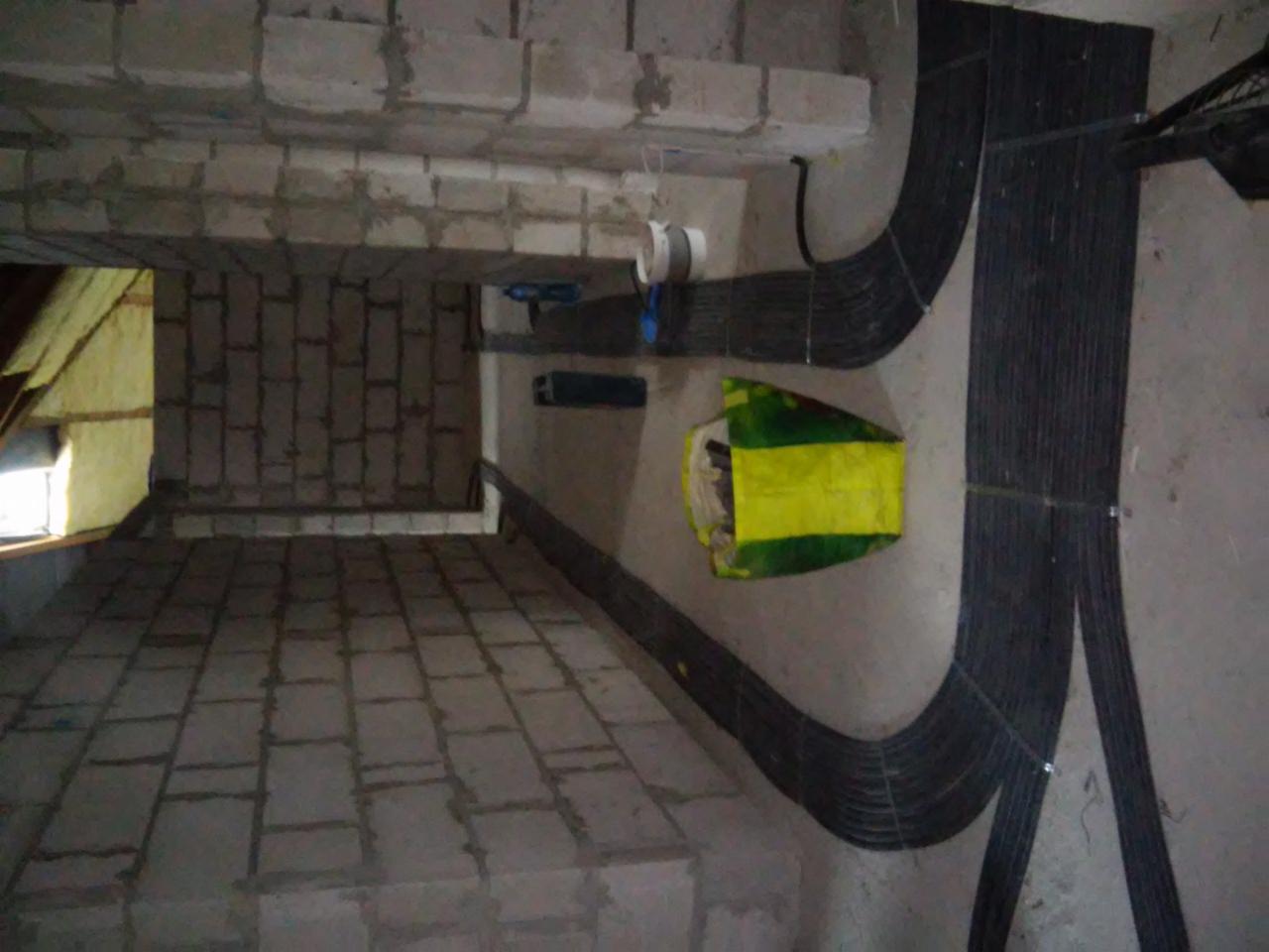 Wiązki kabli elektrycznych ułożone wzdłuż surowych ścian w trakcie instalacji w budynku w stanie deweloperskim, widoczny worek budowlany.