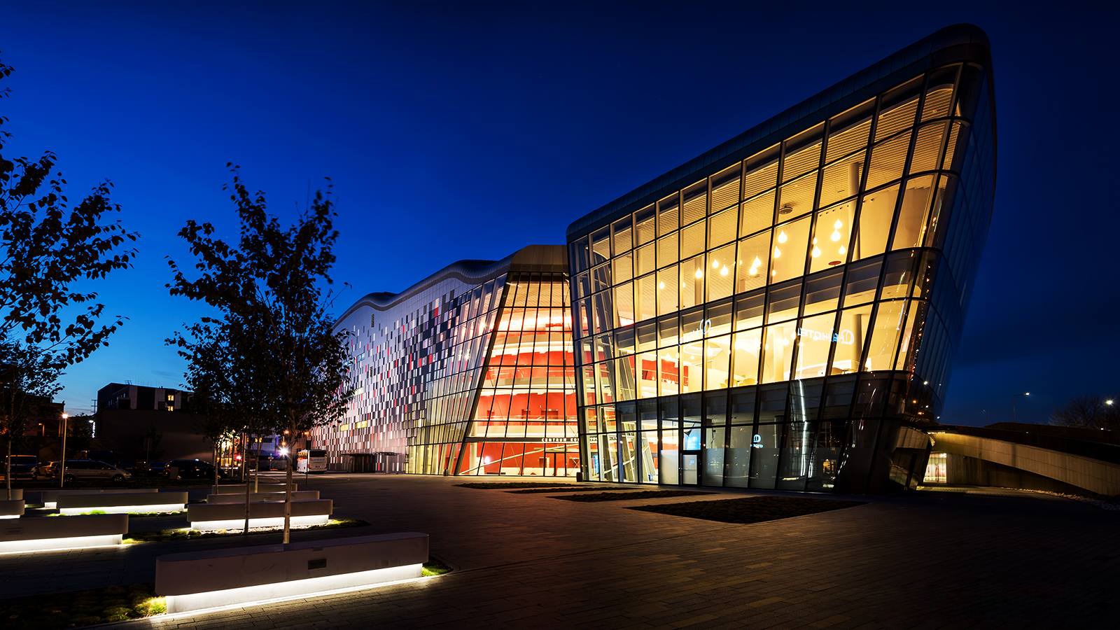 Nowoczesna architektura budynku z przeszkloną fasadą w Olkuszu, oświetlona nocą, z widocznymi detalami elewacji i otoczenia. Kątowe ujęcie podkreśla bryłę budynku.