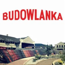 Ekspozycja różnorodnych materiałów budowlanych, w tym dachówek w odcieniach czerwieni i brązu, przed budynkiem hurtowni 'BUDOWLANKA' w Żywcu. Widoczne również elementy architektury budynku...