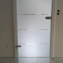 Szklane drzwi wewnętrzne z poziomymi, matowymi pasami i srebrnym uchwytem, zamontowane w nowym, jeszcze nie wykończonym pomieszczeniu z jasnymi płytkami podłogowymi.