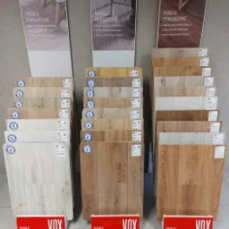 Ekspozycja paneli podłogowych marki VOX w różnych odcieniach drewna, z plakatami prezentującymi aranżacje wnętrz.