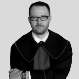 Portret mężczyzny w todze prawniczej, czarno-białe zdjęcie z delikatnym uśmiechem i zegarkiem na nadgarstku, skrzyżowane ręce.