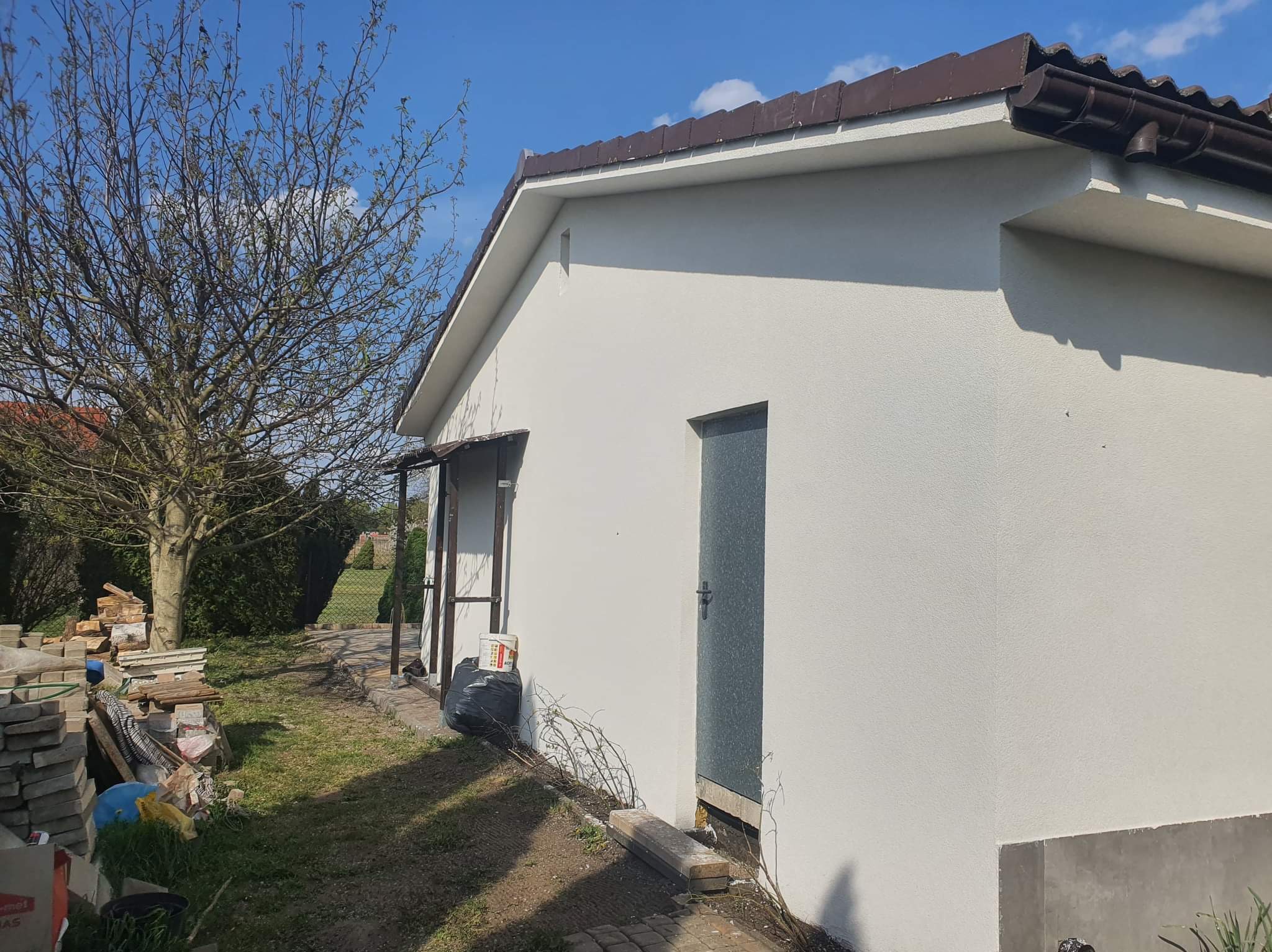 Świeżo otynkowana i pomalowana elewacja budynku gospodarczego w Witkowie, z widocznymi śladami prac wykończeniowych i przygotowanymi materiałami budowlanymi w otoczeniu.