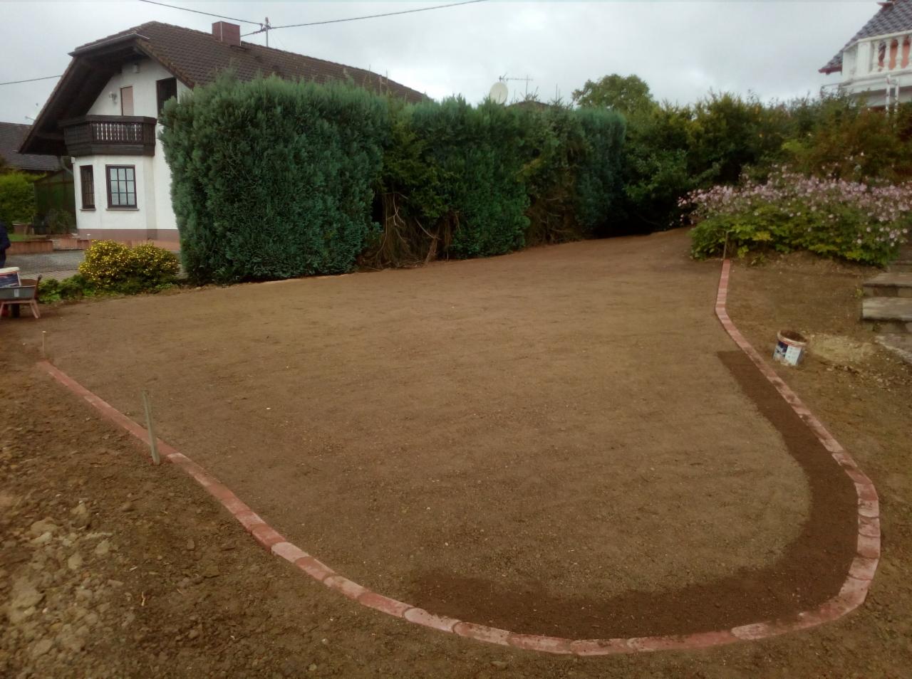 Przygotowany teren pod trawnik z obrzeżem z cegieł, widoczny dom w tle.