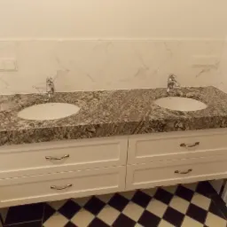 Łazienka z dwoma umywalkami nablatowymi osadzonymi w blacie z szarego konglomeratu, białe szafki z szufladami i podłoga w czarno-białą szachownicę.