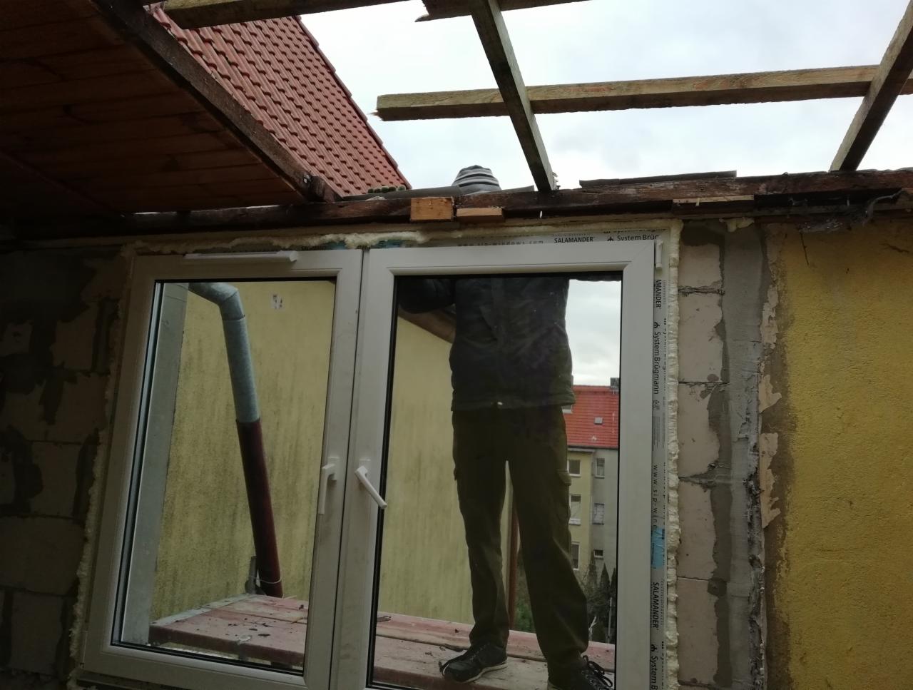 Montaż okna dachowego podczas prac dekarskich, widoczne elementy konstrukcji dachu i fragment rynny