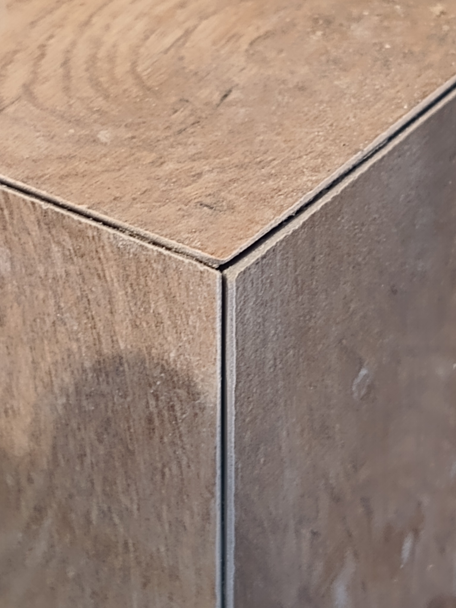 Szczegółowe zbliżenie na narożnik wyłożony brązowymi płytkami imitującymi drewno, z widoczną fugą w kolorze szarym, podkreślającą krawędzie płytek