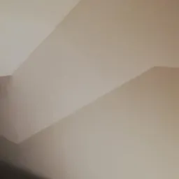 Świeżo wykończona, jasna ściana z widocznym załamaniem sufitu i fragmentem schodów w dolnej części kadru, ukazująca precyzyjne wykończenie powierzchni.