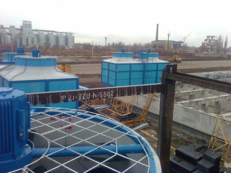 Widok z góry na instalację przemysłową z niebieskimi wieżami chłodniczymi, widoczne silniki, kratownice i elementy konstrukcyjne, w tle silosy i budynki przemysłowe.